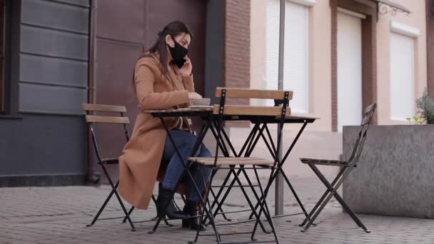 Zakelijke vrouw in het gezicht masker zitten buiten in cafe op terras en werken op laptop — Stockvideo