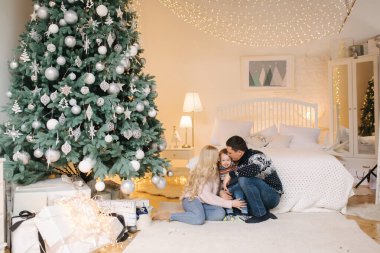 Baba, anne ve oğlunun portresi evde, Noel ağacının yanında yerde oturuyor, hepsi gülümsüyor. Noel ailesi. Mutluluk