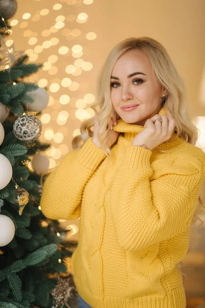 Attraktive junge Mutter am großen Weihnachtsbaum zu Hause. Blonde Haare Frau im Jeans-Pullover Lächeln — Stockfoto