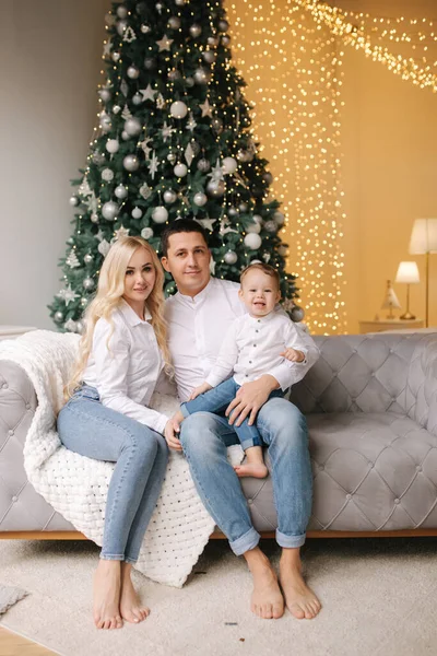 Retrato de pai, mãe e filho sentados no chão em casa perto da árvore de Natal, todos estão sorrindo. Camisas jeans e brancas. Família de Natal. Felicidade — Fotografia de Stock