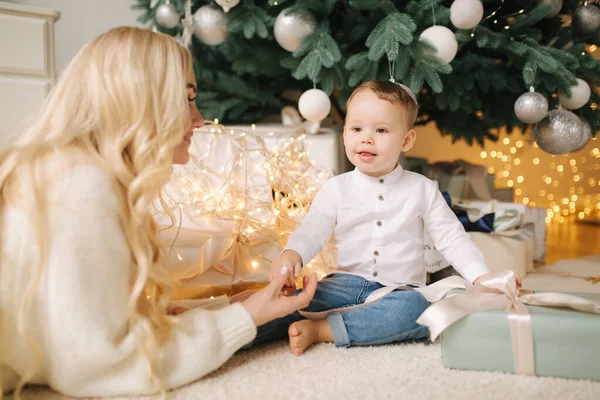 Büyük Noel ağacının yanında hediye arayan sevimli oğluyla güzel bir anne. Mutlu çocuk tatilde ve her anın tadını çıkarıyor. — Stok fotoğraf