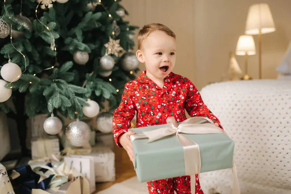 Lindo niño en casa junto al gran árbol de Navidad en busca de regalos. Niño feliz pasar tiempo en vacaciones y disfrutar de cada momento. Solo en casa —  Fotos de Stock
