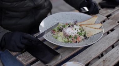 Siyah eldivenli adamın yakınında çatal bıçak takımı var. Qurantine sırasında kafe konsepti. Koruyucu eldivenlerle dışarıda yemek. Taze vejetaryen salatası ve karides.