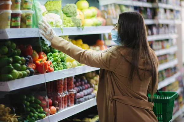 在超级市场，戴着保护膜的快乐女人一边站在食品杂货旁边，一边拿着新鲜蔬菜。漂亮的小女孩拿着菜篮站在旁边选择食物.圣诞购物 — 图库照片
