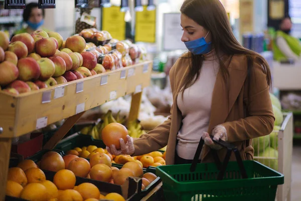 Γυναίκα αγοραστής φοράει προστατευτική μάσκα και γάντια στο σούπερ μάρκετ. Ψώνια κατά τη διάρκεια της πανδημίας. Γυναίκα που αγοράζει φρέσκα φρούτα — Φωτογραφία Αρχείου