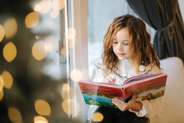 圣诞假期，漂亮的小女孩在窗台上看书 — 图库照片