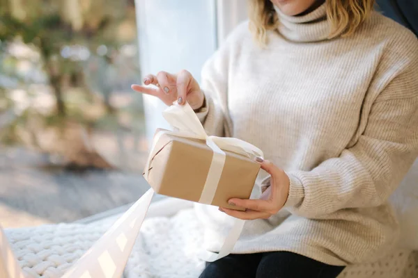 Primer plano de la mujer en sudadera con capucha abierta presente en el momento de Navidad. Mujer elegante de pie junto al gran árbol de Navidad en frente de la ventana — Foto de Stock