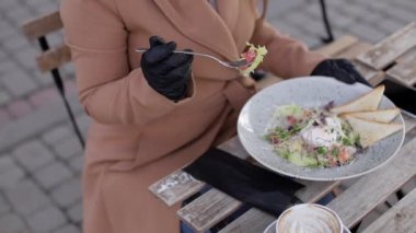 Terastaki kafede öğle yemeği yiyen güzel genç bir kadın. Siyah koruyucu maskeli bir kadın. Kadın yemek yerken maskesini çıkarıyor.