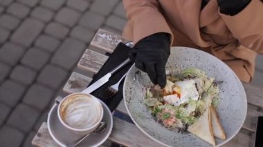 Siyah eldivenli çekici genç bir kadının elinde çatal bıçak takımı var. Qurantine sırasında kafe konsepti. Koruyucu eldivenlerle dışarıda yemek. Taze vejetaryen salatası ve karides.