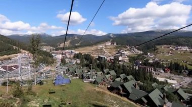 Güneşli bir sonbahar günündeki kayak merkezinin asansör kabinlerinin manzarası. Yeşil çimlerin üzerinde kaldırma hareketi. Ormanda yavaşça teleferik hareket ediyor. Tatil turizmi tatili kavramı