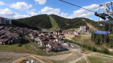 Güneşli bir sonbahar günündeki kayak merkezinin asansör kabinlerinin manzarası. Yeşil çimlerin üzerinde kaldırma hareketi. Ormanda yavaşça teleferik hareket ediyor. Tatil turizmi tatili kavramı
