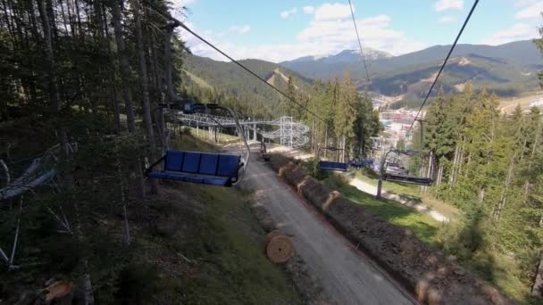 Θέα από το χιονοδρομικό κέντρο καμπίνες ανελκυστήρα σε ένα βουνό ηλιόλουστη μέρα του φθινοπώρου. Ανυψώστε κίνηση πάνω από πράσινο γρασίδι. Αργά κίνηση του τελεφερίκ στο δάσος. Concept διακοπές ταξίδια τουριστικές διακοπές — Αρχείο Βίντεο
