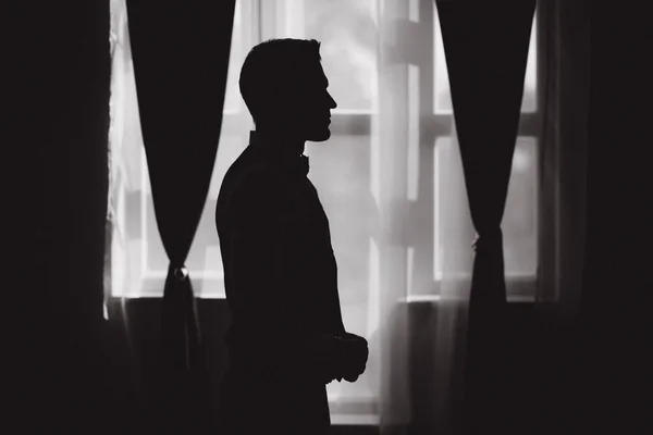 Silhouette of handsome groom in hotel stand by in front of the window — Stock Photo, Image