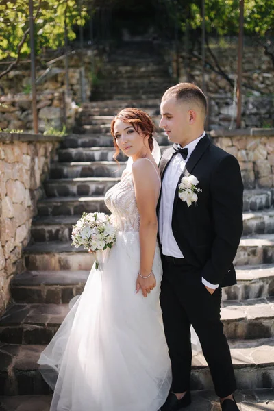 Прекрасная невеста со своим красивым женихом, выходящим на улицу в день свадьбы. Счастливых молодоженов. Фон виноградного поля — стоковое фото