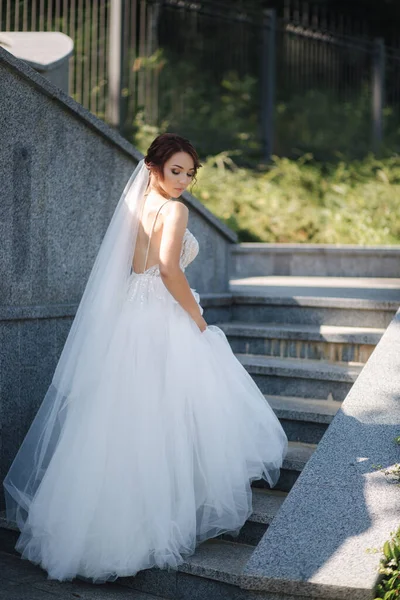 Gorgeous bride in elegant dress outdoors. Fashion model go upstairs