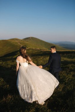 Damat ve gelin dağlardaki tepede. Green Hill 'in önünde bir düğün çifti. Yeni evliler, güzel bir yaz gününde gün batımında dağlarda romantik anların tadını çıkarıyorlar.