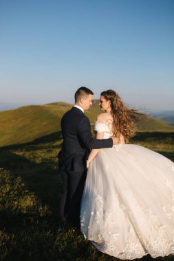 Damat ve gelin dağlardaki tepede. Green Hill 'in önünde bir düğün çifti. Yeni evliler, güzel bir yaz gününde gün batımında dağlarda romantik anların tadını çıkarıyorlar.