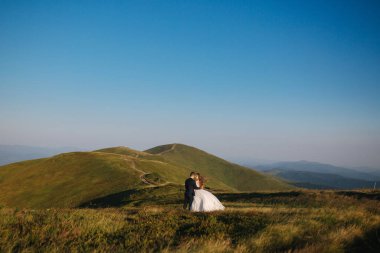 Damat ve gelin dağlardaki tepede. Green Hill 'in önünde bir düğün çifti. Yeni evliler, güzel bir yaz gününde gün batımında dağlarda romantik anların tadını çıkarıyorlar.