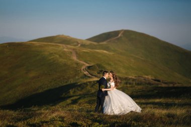 Damat ve gelin dağlardaki tepede. Green Hill 'in önünde bir düğün çifti. Yeni evliler, güzel bir yaz gününde gün batımında dağlarda romantik anların tadını çıkarıyorlar.