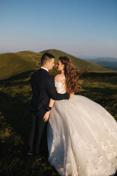 Vőlegény és menyasszony a hegyekben. Esküvői pár Green Hill előtt. Friss házasok élvezik a romantikus pillanatokat a hegyekben naplementekor a gyönyörű nyári napon — Stock Fotó