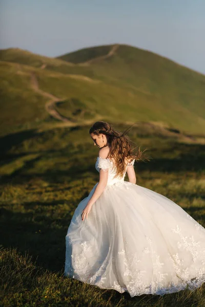 美しい若い花嫁は山の中の丘の上に立つ。風の強い屋外。背景に緑の丘 — ストック写真