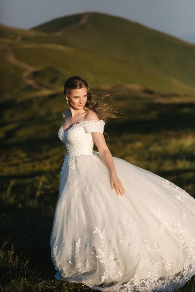 Schöne junge Braut steht auf dem Hügel in den Bergen. Windig im Freien. Grüne Hügel im Hintergrund — Stockfoto