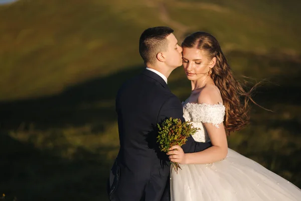 Ritratto di sposa attraente e sposo elegante godendo momenti romantici in montagna al tramonto nella bella giornata estiva. Matrimonio. Colline verdi sullo sfondo — Foto Stock