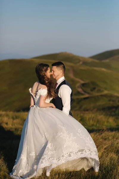 Vőlegény és menyasszony a hegyekben. Esküvői pár Green Hill előtt. Friss házasok élvezik a romantikus pillanatokat a hegyekben naplementekor a gyönyörű nyári napon — Stock Fotó
