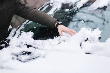 Yakışıklı adam elleri kullanarak arabasını kardan temizliyor. Kış açık havada