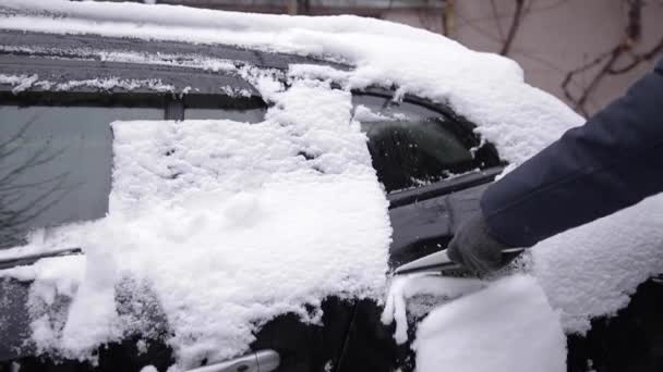 Zbliżenie człowieka czyści śnieżne okno na samochodzie ze skrobakiem śnieżnym. Skup się na skrobaku. Zimny śnieżny i mroźny poranek. Czarny samochód — Wideo stockowe