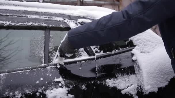 Närbild av människan är rengöring snöiga fönster på en bil med snöskrapa. Fokusera på skrapan. Kall snöig och frostig morgon. Svart bil — Stockvideo