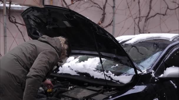Mężczyzna otwiera maskę samochodu i próbuje dowiedzieć się, co się stało z samochodem. Zima na zewnątrz — Wideo stockowe