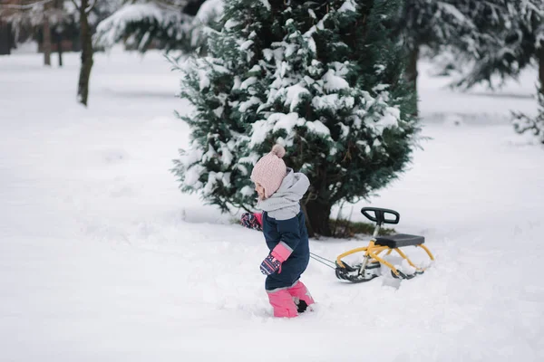 Κοριτσάκι που περπατάει στο χιόνι και σηκώνει τα έλκηθρα της. Ενεργός ελεύθερος χρόνος σε εξωτερικούς χώρους το χειμώνα. Γλυκό κοριτσάκι. — Φωτογραφία Αρχείου