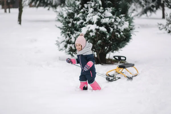 Kleines Mädchen läuft auf Schnee und zieht ihre Schlitten hoch. Aktive Freizeit im Freien im Winter. Niedliches kleines Mädchen — Stockfoto