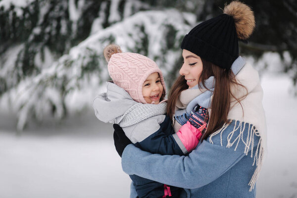 Beautiful young mom with her cute daughter in winter park. Christmas time