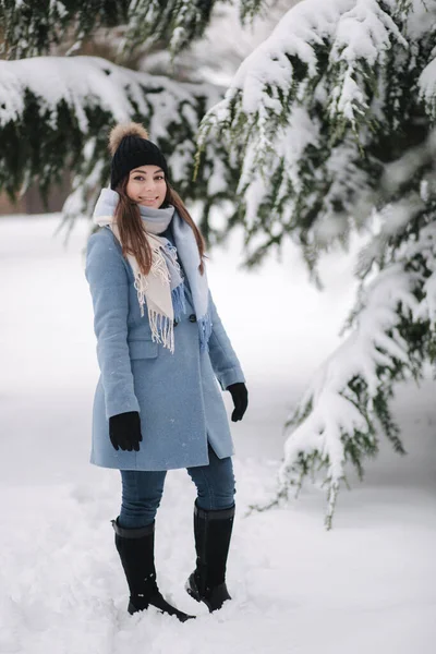 Красива жінка в блакитному пальто, що йде в лісі в зимовий сніжний день. Красива жінка позує з фотографом — стокове фото