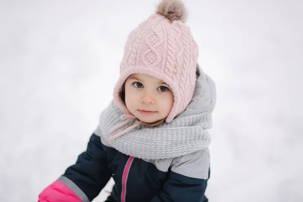 Menina feliz andando no parque na neve. Menina adorável em um chapéu rosa e macacão andando na floresta em um dia nevado de inverno — Fotografia de Stock