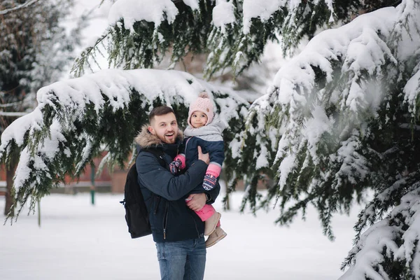 Adorável filhinha com seu adorável pai ficar ao lado da grande árvore nevada. Menina bonito ri — Fotografia de Stock