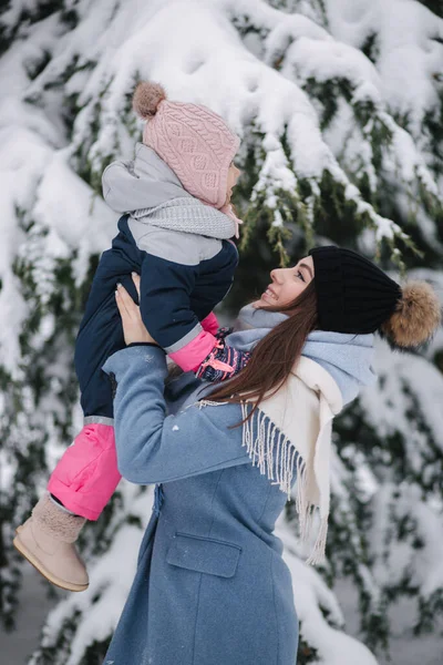 Krásná mladá maminka se svou roztomilou dcerou v zimním parku. Vánoce. Pozadí zasněženého stromu — Stock fotografie