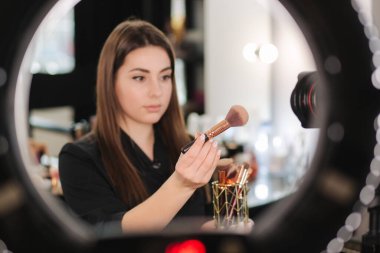 Genç güzel kadın ve profesyonel güzellik makyaj sanatçısı vlogger makyaj dersini internet sitesinde ya da sosyal medyada paylaşmak için kayıt ediyor. Blogcu tripod ve halka lambasında dijital kamera kullan