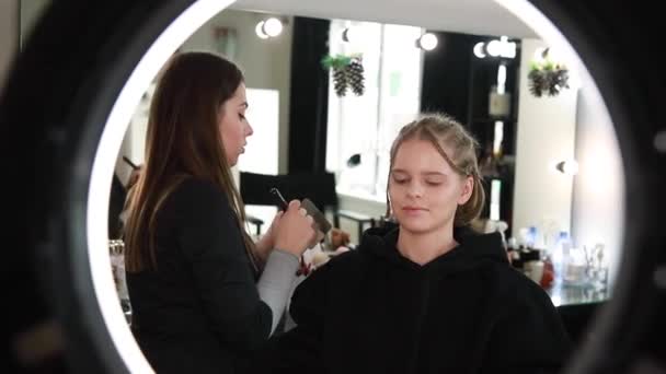 Γυναίκα κάνει μακιγιάζ για ελκυστική ξανθιά γυναίκα μαλλιά στο στούντιο. Βίντεο από makeup artist εφαρμογή καλλυντικών για όμορφο μοντέλο. Ψηφιακή κάμερα κάνει βίντεο για vlog — Αρχείο Βίντεο