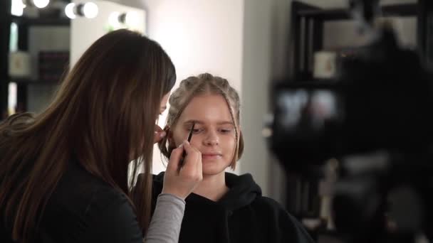 Mujer maquillaje para el cabello rubio atractivo mujer en el estudio. Video de maquillador aplicando cosméticos para hermosa modelo. Cámara digital de vídeo para vlog — Vídeo de stock