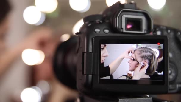 Kobieta zrobić makijaż dla atrakcyjnej blond włosy kobieta w studio. Selektywna ostrość aparatu cyfrowego z makijażystą stosującym kosmetyki do pięknego modelu. Vlog — Wideo stockowe