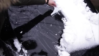 Bir adam kar kazıyıcı ile bir arabanın karlı camını temizliyor. Kazıyıcıya odaklan. Soğuk, karlı ve soğuk bir sabah. Siyah araba.