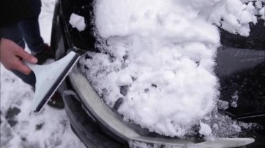 Bir adam kar kazıyıcı ile bir arabanın karlı camını temizliyor. Kazıyıcıya odaklan. Soğuk, karlı ve soğuk bir sabah. Siyah araba.