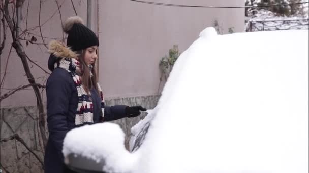 Kobieta czyści śnieżne okno w samochodzie ze skrobakiem śnieżnym. Ładna kobieta Warmy ubrana w czysty samochód na zewnątrz. Zimny śnieżny i mroźny poranek. Czarny samochód — Wideo stockowe