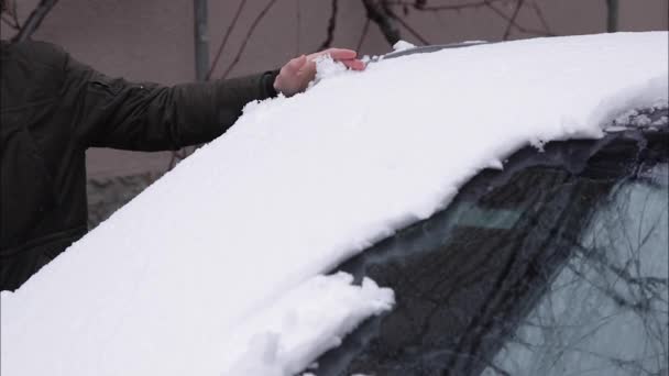 Snygg man rengör sin bil från snö med hjälp av händer. Vinter utomhus — Stockvideo