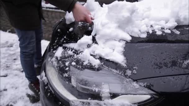 Zbliżenie człowieka czyści śnieżne okno na samochodzie ze skrobakiem śnieżnym. Skup się na skrobaku. Zimny śnieżny i mroźny poranek. Czarny samochód — Wideo stockowe