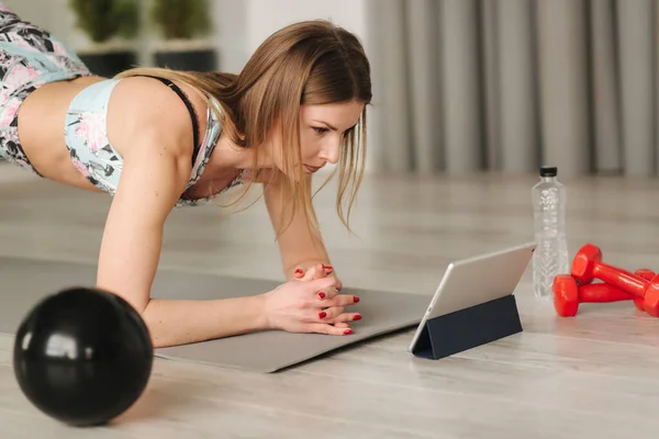 Spor giyimli atletik kadın evde egzersiz yapıyor. Kadınlar diong egzersizleri yaparken tablete bakarlar. Spor ve eğlence konsepti. Sağlıklı yaşam tarzı — Stok fotoğraf
