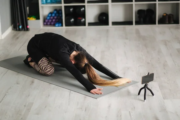 Genç yoga ustası, internetteki kursu için cep telefonuyla yaptığı egzersizin video içeriğini kaydediyor. Stüdyoda atletik kadın eğitimi — Stok fotoğraf